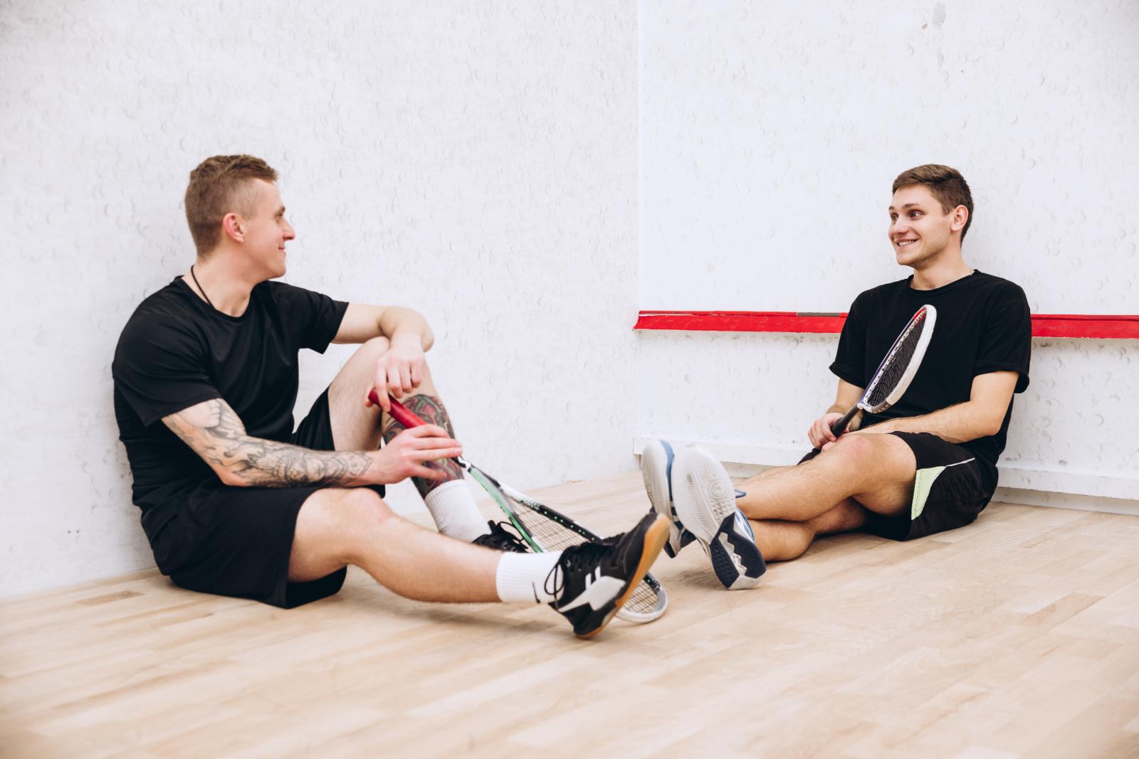 Zwei Spieler sitzen nach dem Spiel entspannt an der Wand des Courts und unterhalten sich